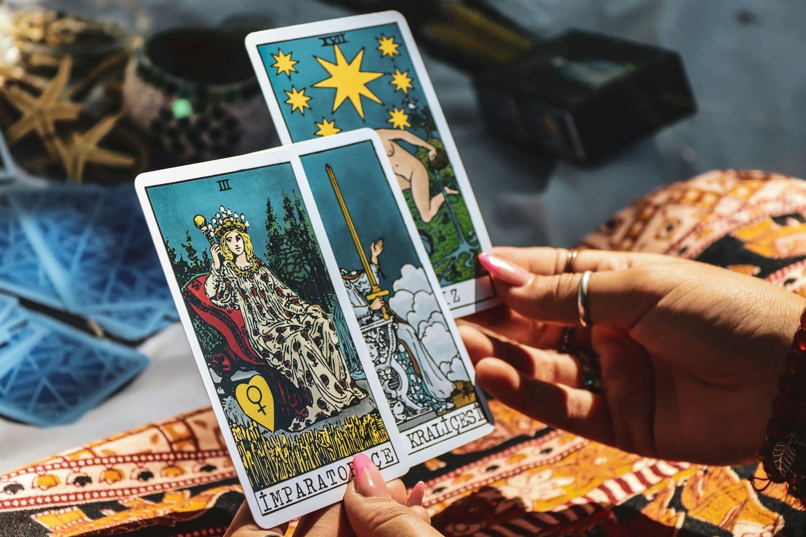 Desenli örtü üzerinde elde yelpaze gibi açılmış üç tarot kartı